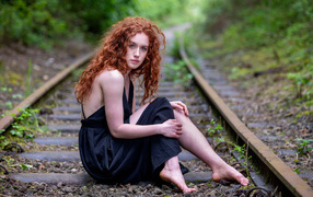 Red-haired girl in a black dress sits on the paths
