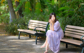 Грустная девушка азиатка в платье на лавке в парке 