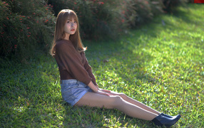 Грустная девушка азиатка сидит на зеленой траве 
