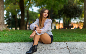 Грустная девушка сидит на земле в парке 