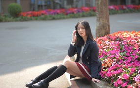 Schoolgirl girl sitting on the ground near the flower bed