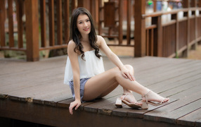 Улыбающаяся девушка азиатка сидит на мосту 