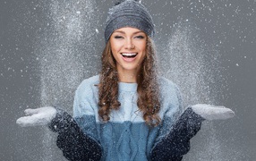 Улыбающаяся девушка ловит снег руками на сером фоне