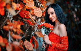 Улыбающаяся девушка с букетом гвоздик у стены с осенними листьями