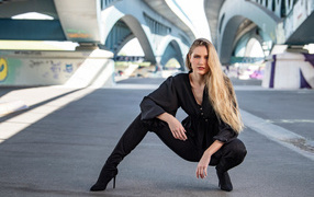 Стильная девушка в черном костюме под мостом