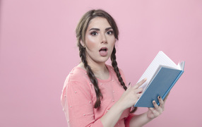 Удивленная девушка с книгой на розовом фоне