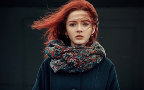 Ветер развивает волосы рыжеволосой девушки в пальто