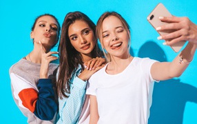 Three female friends take a selfie on a blue background