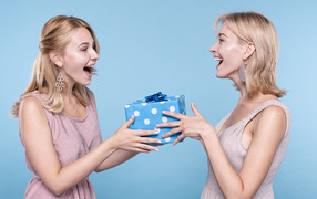 Two blonde girlfriends with a gift on a blue background