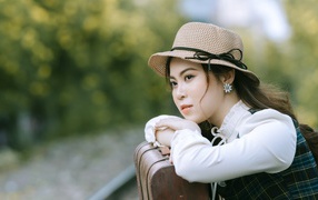 Молодая азиатка в шляпе с чемоданом