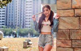 Молодая азиатка в коротких шортах стоит у стены