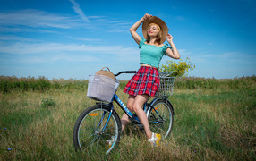 Молодая девушка на велосипеде на поле под голубым небом 