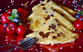 Thin pancakes with cherries and blueberries on a red carnival background