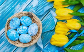Painted eggs and a bouquet of yellow tulips on a blue background for Easter