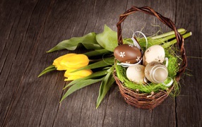 Маленькая корзина с пасхальными  яйцами на столе с тюльпанами