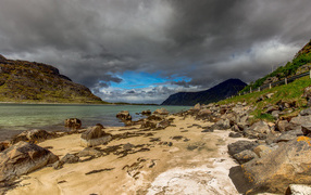Big stones on the shore of the fjord under a stormy sky