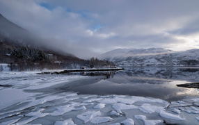 Покрытое льдом холодное озеро у гор в тумане