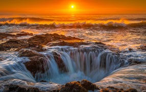 Ocean water flows into a hole at sunset
