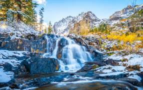The waterfall flows down the snow-covered rocks in the mountains