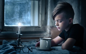 Маленький мальчик сидит за столом при свете свечи 