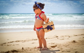 Маленькая девочка в купальнике гуляет по пляжу 