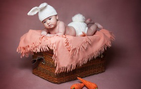 Маленький ребенок в костюме зайчика лежит на корзине 