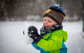 Веселый маленький мальчик со снегом в руках 