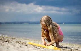 Little blonde girl playing on the sand by the sea