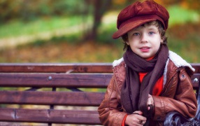 Little boy in a cap sits on a bench