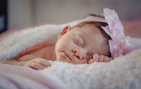 Маленькая грудная девочка с цветком на голове на кровати 