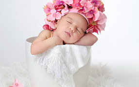 Маленький ребенок в шапке с цветами в горшке 