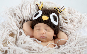 Маленький ребенок  в вязаной шапке спит на кровати 