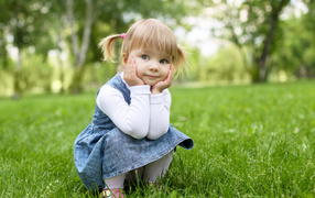 Маленькая девочка в сарафане сидит на траве 