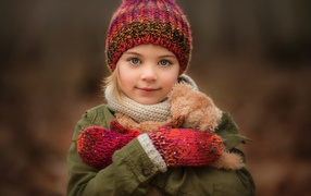 Маленькая девочка в теплой шапке и варежках  с игрушкой в руках 