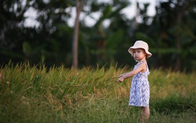 Little girl with a panama on her head stands in the grass