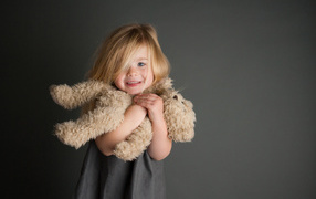 Маленькая девочка с игрушечным медвежонком в руках  на сером фоне 