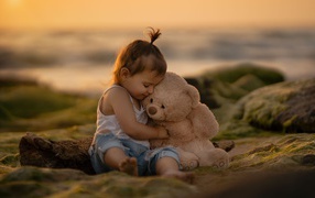 Маленькая девочка с игрушечным медведем сидит на камне