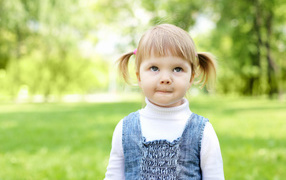 Маленькая девочка с хвостиками на голове в парке 
