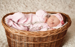 Маленькая новорожденная девочка в розовом костюме спит в корзине 