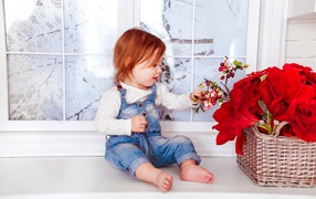 Little red-haired girl sitting by a basket of flowers