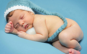 Маленький спящий ребенок в шапке на голубом фоне 