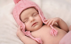 Маленький спящий ребенок в розовой вязаной шапке 