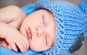 Маленький спящий грудной ребенок в голубой вязаной шапке 