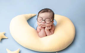 Sleeping nursing baby wearing glasses on a yellow pillow