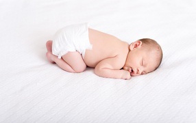 Маленький грудной ребенок в памперсе спит на белом фоне