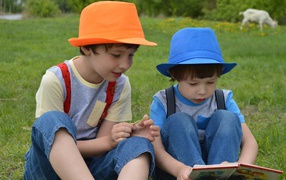 Два мальчика с книгой сидят на траве