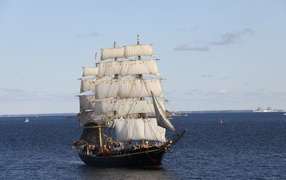 Large black ship with white sails at sea