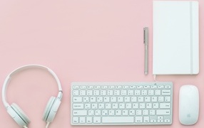 Headphones, keyboard, notepad with pen and mouse on a pink background