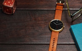 Men's wristwatch on a wooden table with a notepad and glasses