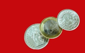 Три монеты швейцарских франков на красном фоне